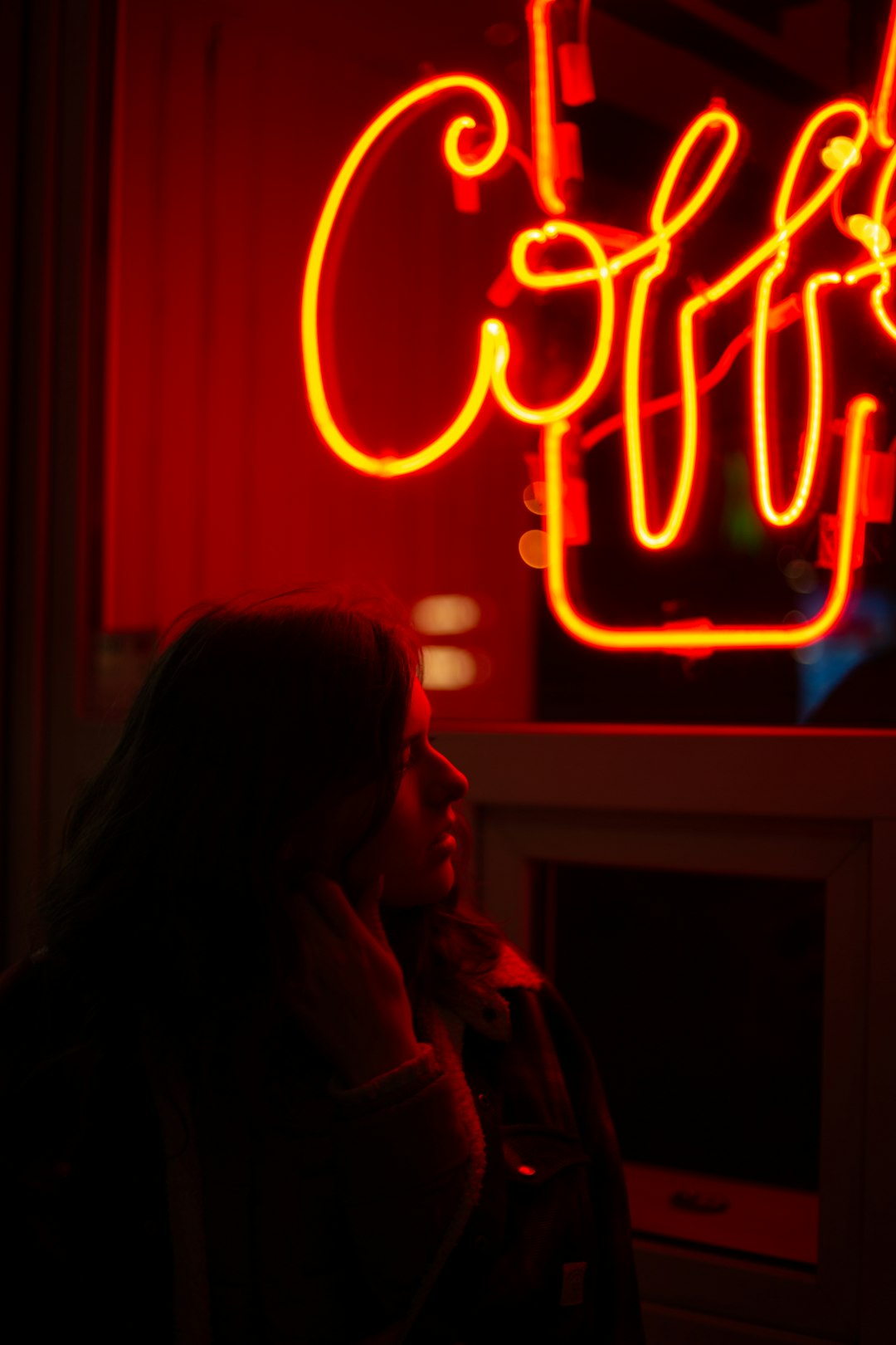 woman in gray hoodie standing near red and yellow neon light signage