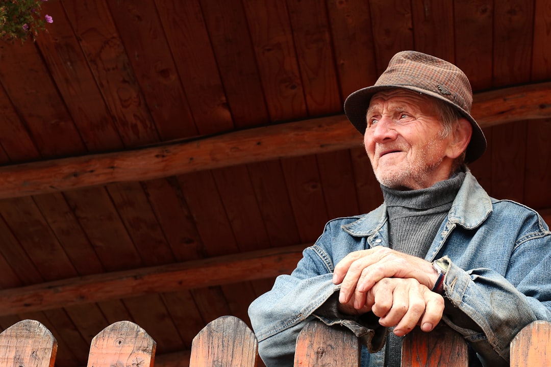 man in blue denim jacket and brown fedora hat sitting on brown wooden bench