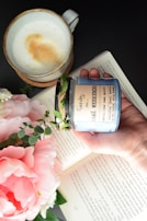 A candle nestled in a rustic ceramic holder beside an open book and a cup of tea.