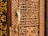A detailed view of a wooden door with intricate carvings featuring geometric patterns and a prominent golden door handle shaped like a bird. The craftsmanship highlights traditional and ornate design elements.