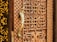 A detailed view of a wooden door with intricate carvings featuring geometric patterns and a prominent golden door handle shaped like a bird. The craftsmanship highlights traditional and ornate design elements.