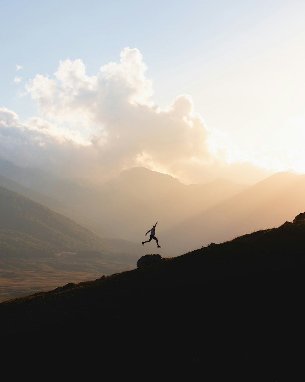 silhouette of person jumping on mountain during daytime