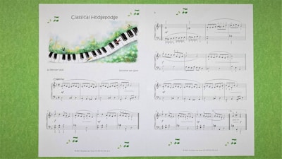 A sheet of classical music titled 'Classical Hodgepodge' is displayed, featuring a whimsical illustration of a piano keyboard flowing through a grassy landscape. The sheet contains musical notes and compositions on a white background, with additional decorative musical notes around the edges. The pages are set against a light green textured background.