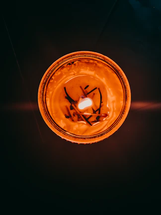 A close-up of a golden soy candle with a flickering wooden wick, casting soft shadows.
