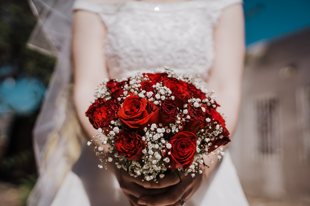 donna in abito da sposa bianco che tiene mazzo di rose rosse
