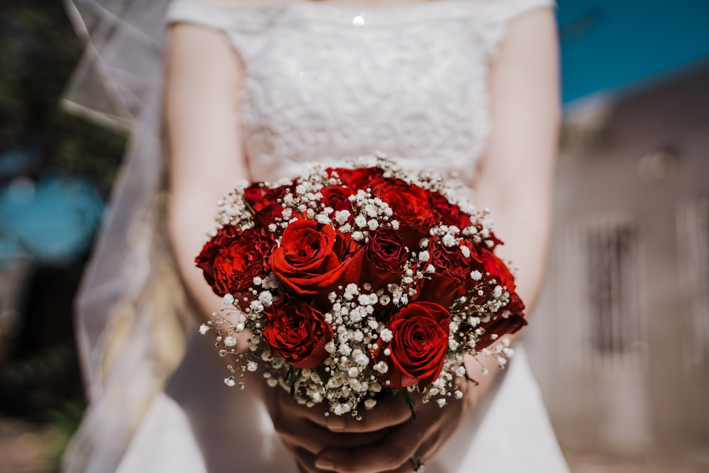 woman in white wedding dress holding bouquet of red roses