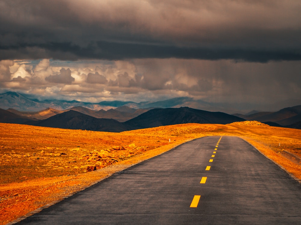 black asphalt road near brown mountains under gray clouds during daytime