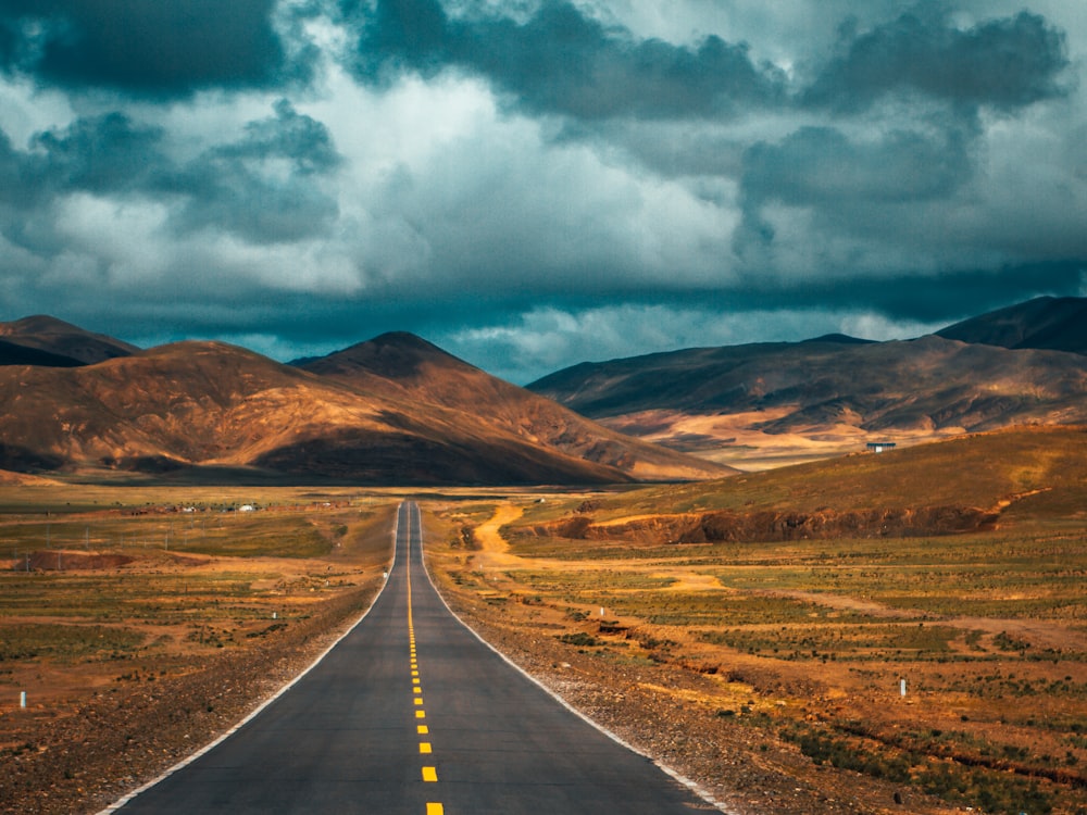 Carretera de hormigón gris cerca de la montaña marrón bajo nubes blancas y cielo azul durante el día