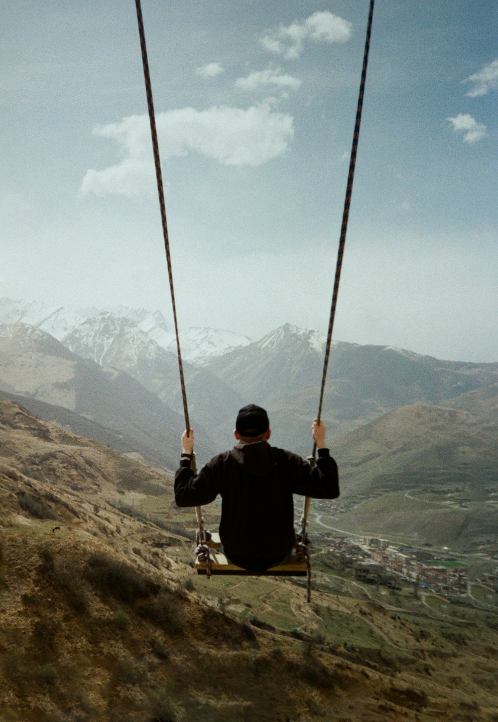man in black jacket sitting on swing over the mountain during daytime