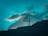 A majestic snow-capped mountain peak against a vibrant teal sky, partially covered by soft clouds.