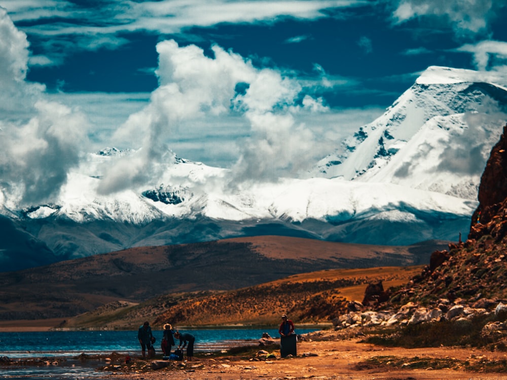 people standing on brown field near mountain under white clouds during daytime