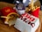 A wooden surface is topped with fast food items including two packages of French fries in red packaging, a wrapped bacon burger in purple wrapping, and a closed Big Mac box. The scene is typical of a fast-food meal setting.