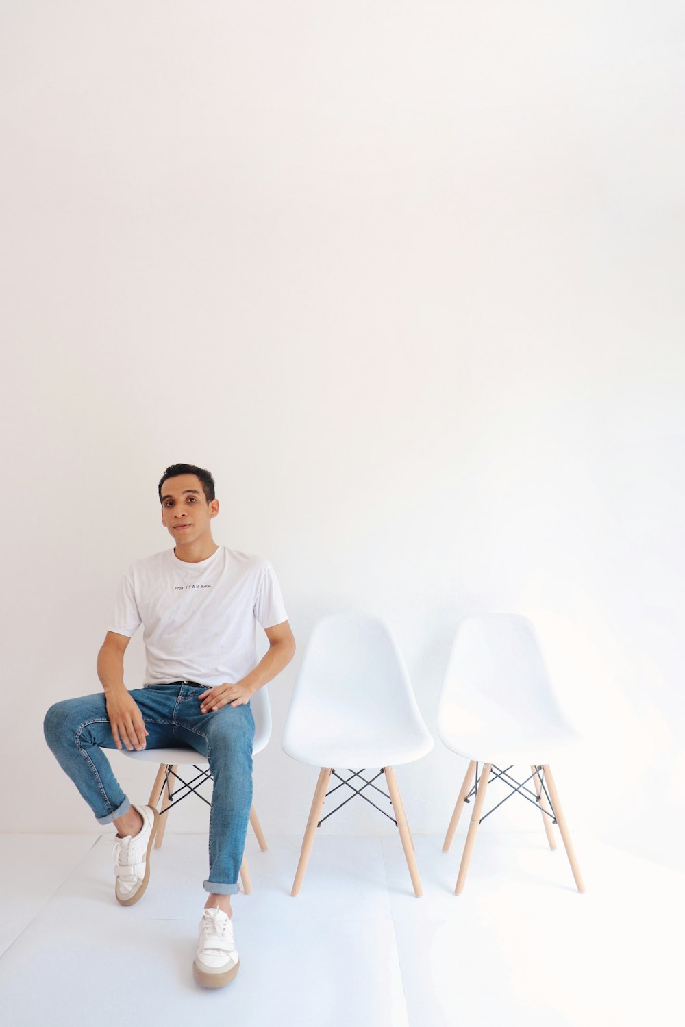 man in white crew neck t-shirt and blue denim jeans sitting on white chair