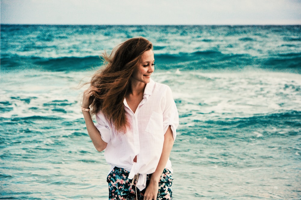 昼間のビーチに立つ白いドレスシャツの女性