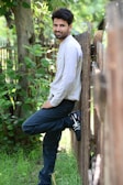 A smiling high school senior leaning against a rustic wooden fence.