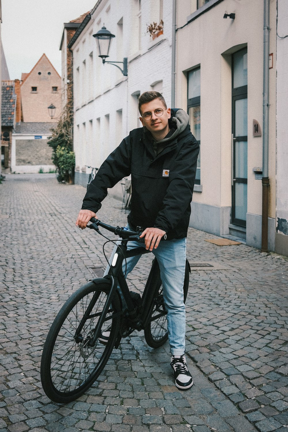 man in black jacket and blue denim jeans riding on black bicycle