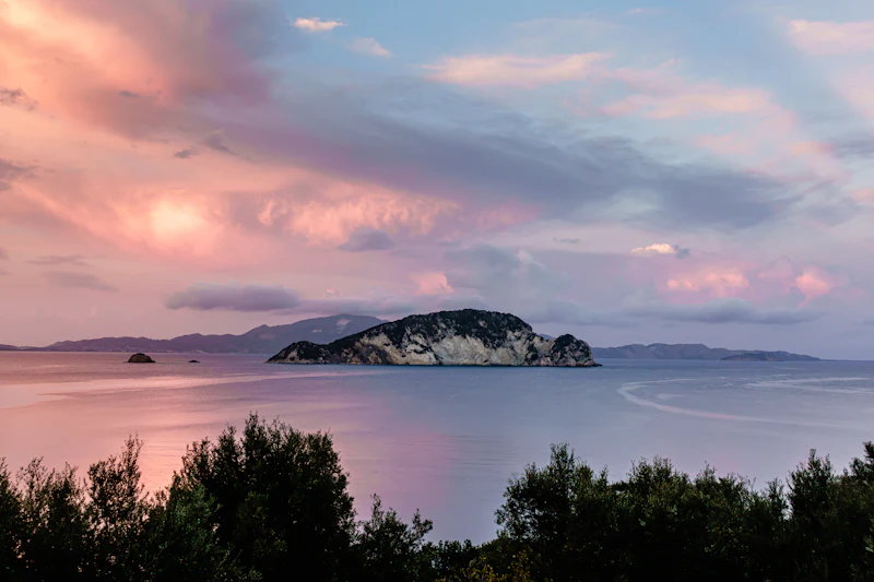 A pink sunset sky over the sea and a small island