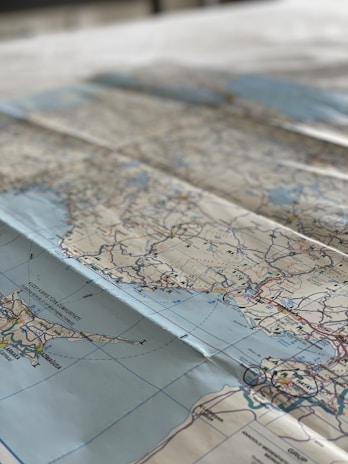 A detailed geographical map spread out on a flat surface, showing a large area with various landmarks and colored lines indicating roads and borders. The map appears to focus on a coastal region with nearby bodies of water and numerous labeled cities.