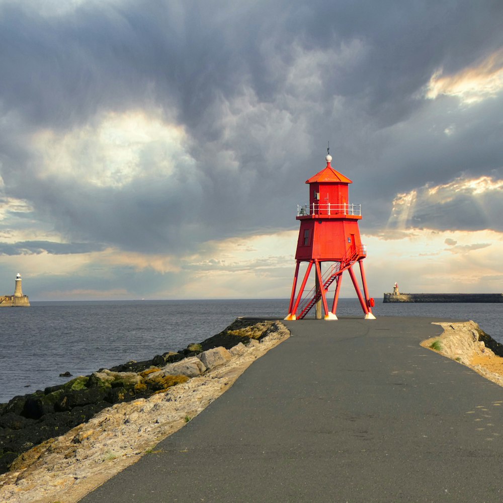 red and white lighthouse near body of water under cloudy sky during daytime