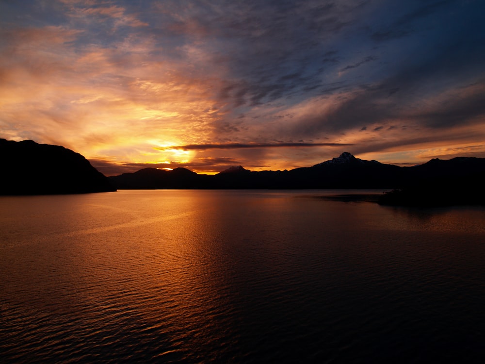 silhouette of mountain near body of water during sunset