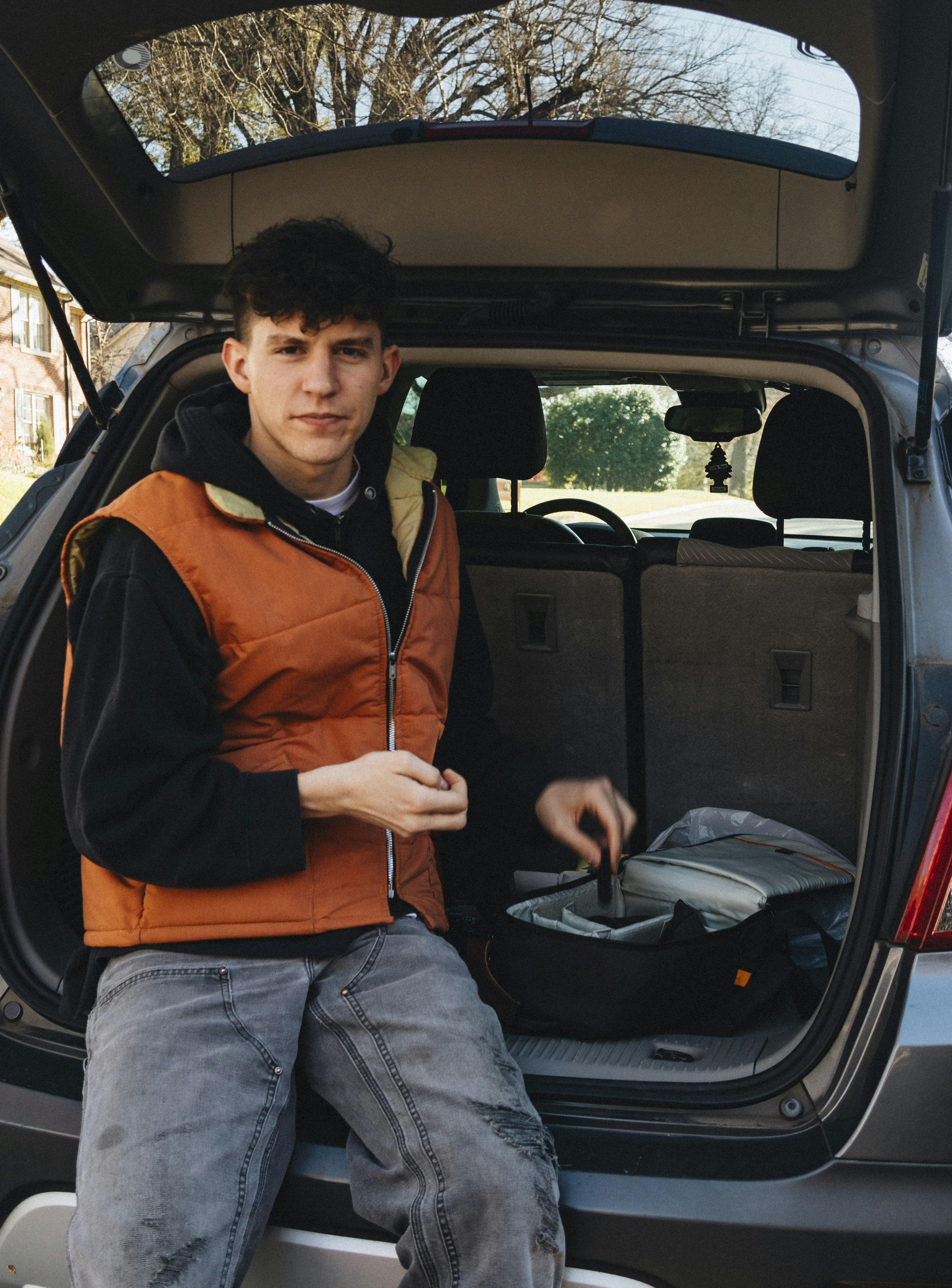 man in orange and black jacket and blue denim jeans sitting on car seat