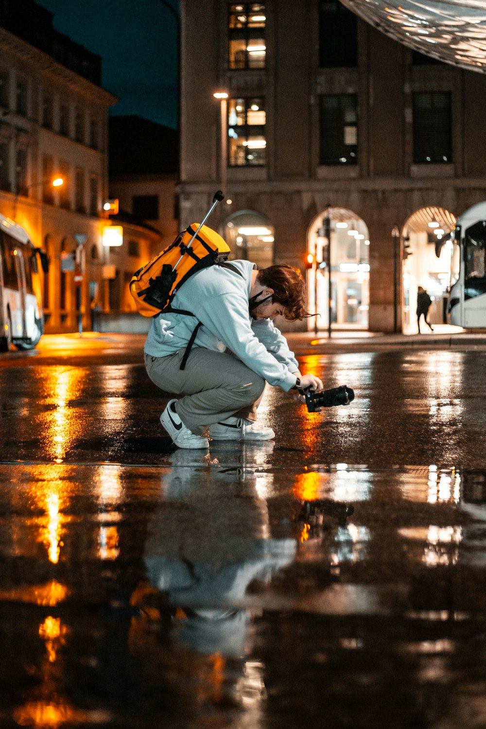 man in white jacket and black pants sitting on sidewalk during night time