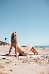 woman in black bikini lying on beach sand during daytime