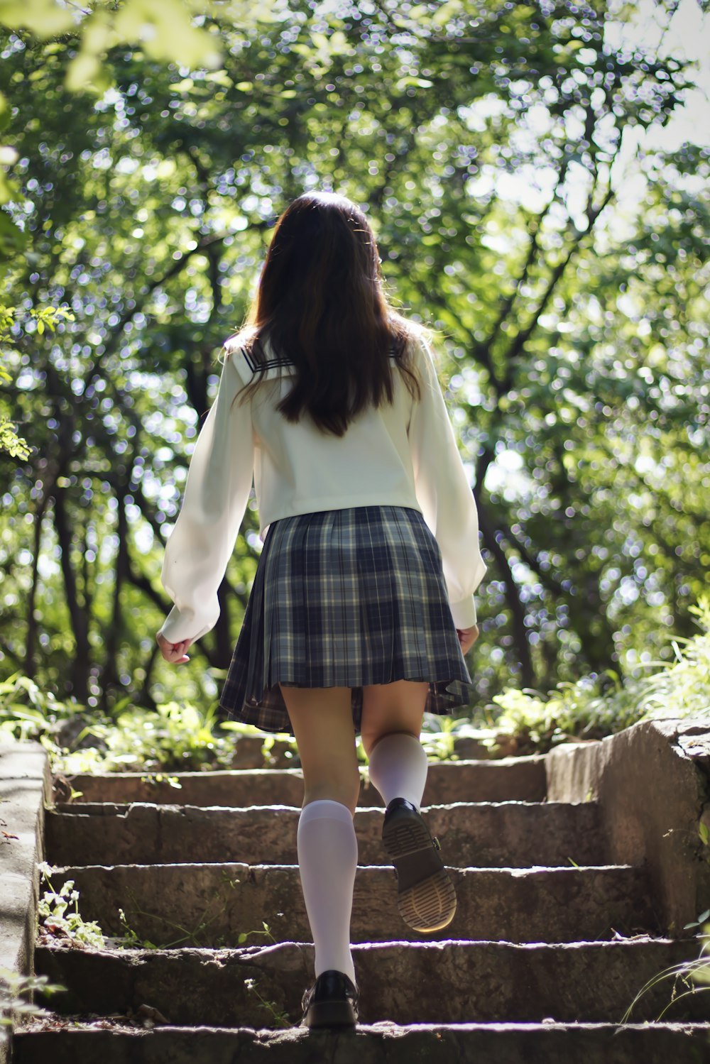 woman in white long sleeve shirt and blue and black plaid skirt standing on brown concrete