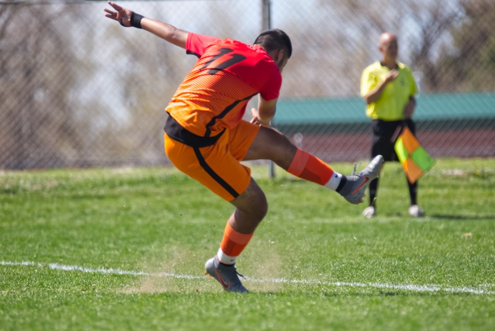 man in orange jersey shirt kicking soccer ball on green grass field during daytime