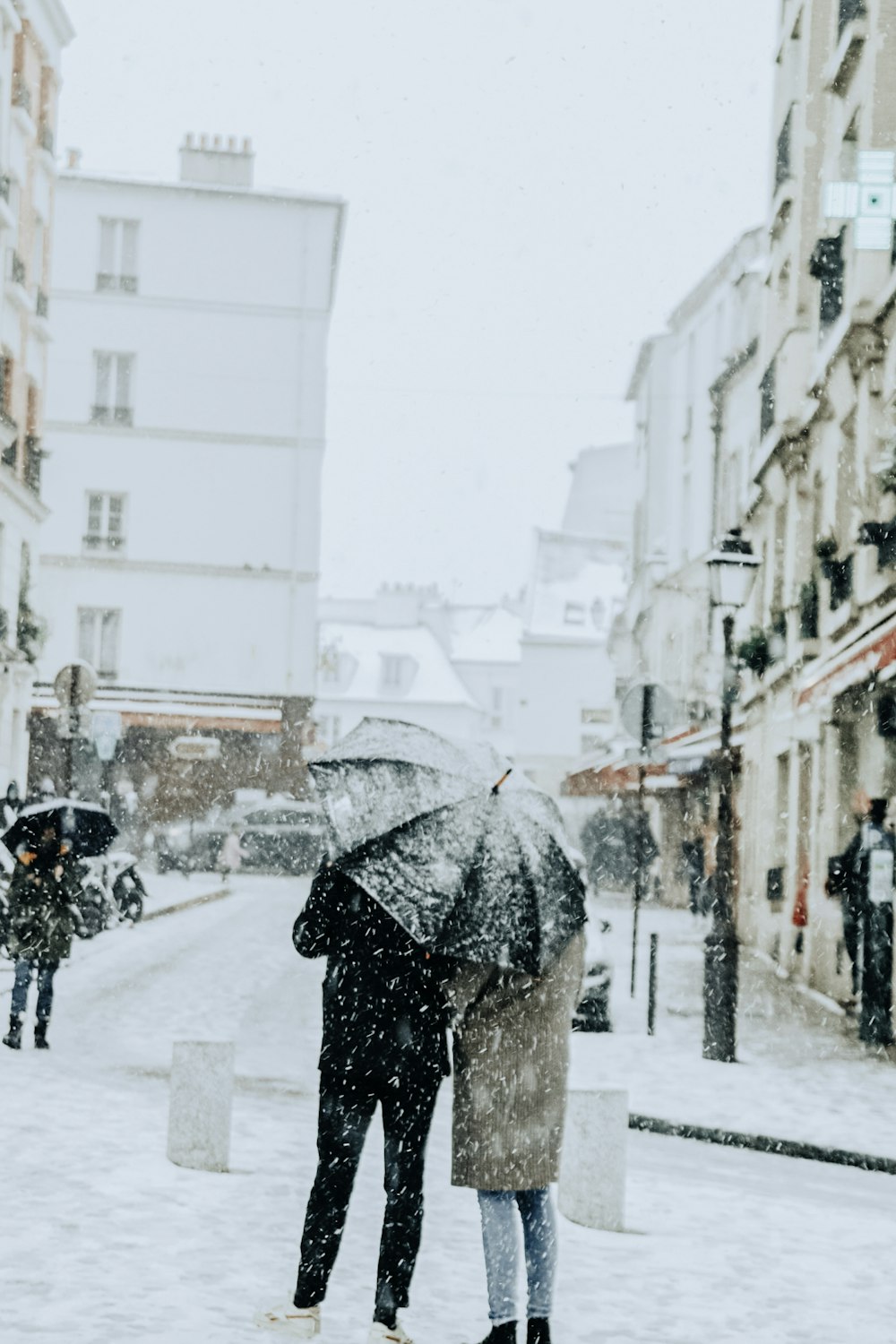 person holding black umbrella walking on snow covered road during daytime