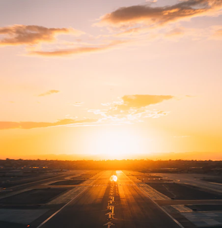 An aerial view of a runway at sunset, with golden light reflecting off the tarmac.