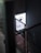 A dimly lit industrial stairwell with a metal mesh railing is partially illuminated by a glowing rectangular sign. The sign has a minimalist design featuring a circle with an orbit-like line and the words 'START BASE NONOS STORY INSPIRA' in a contemporary font.