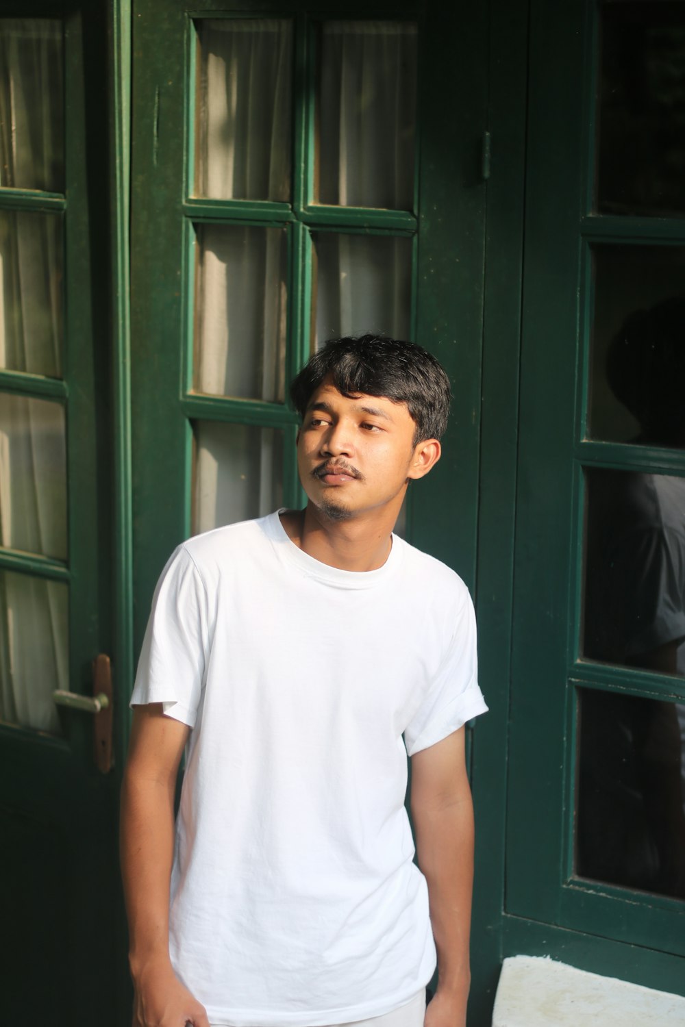 man in white crew neck t-shirt standing near green wooden door