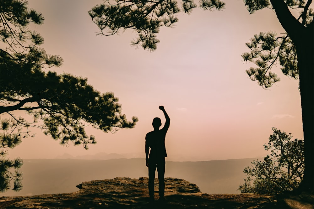 silhouette of woman standing on rock formation near body of water during sunset