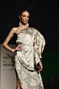 A graceful plus-size model wearing a sleek, gold-accented dress against a soft white background.