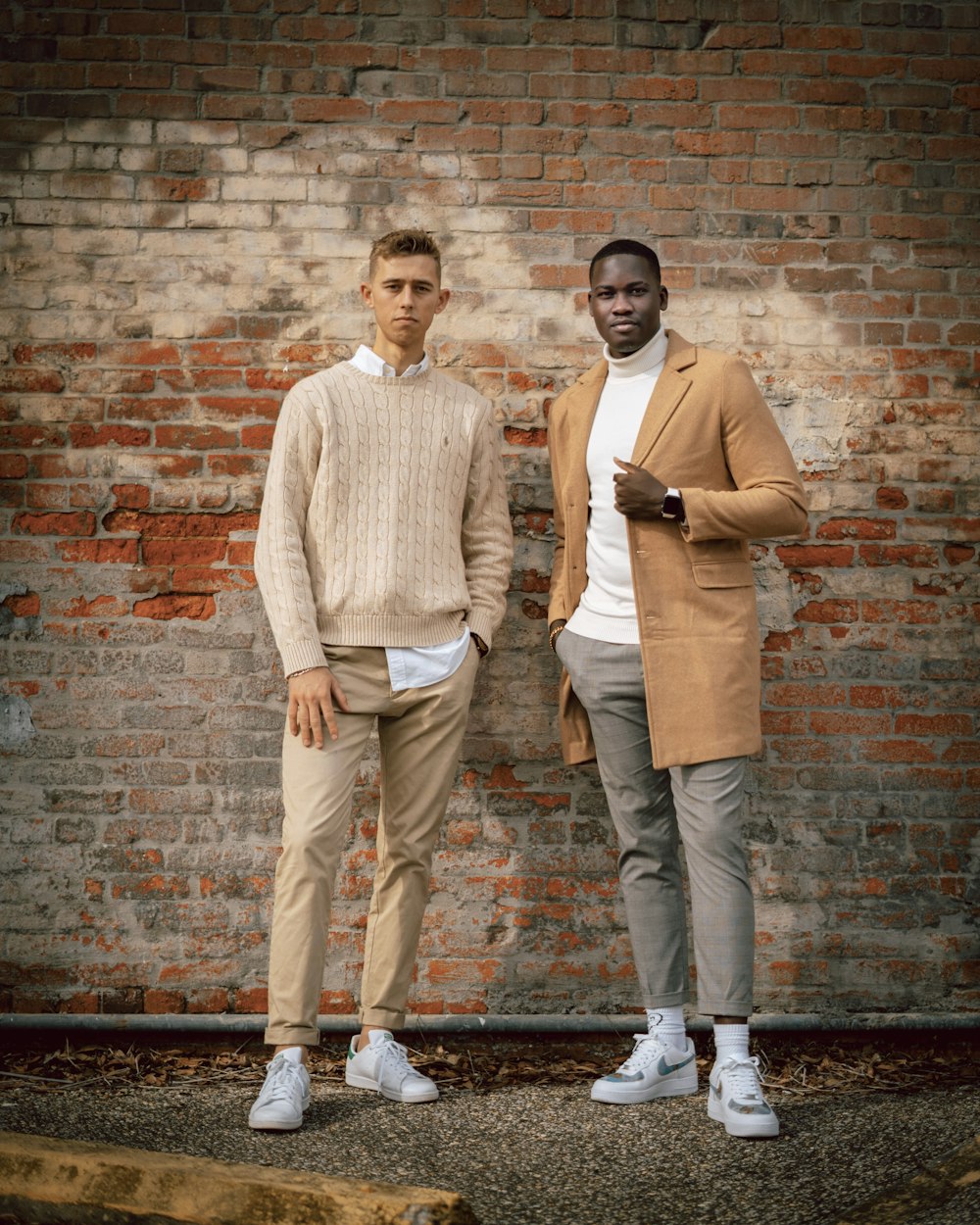 man in white dress shirt and brown pants standing beside brown brick wall