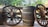 Wooden wagon wheels are placed on either side of a large wooden barrel with the text 'Beer 50 plus' written on it. The setting is outdoors, with a backdrop of lush green trees and a body of water visible in the background.