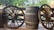 Wooden wagon wheels are placed on either side of a large wooden barrel with the text 'Beer 50 plus' written on it. The setting is outdoors, with a backdrop of lush green trees and a body of water visible in the background.