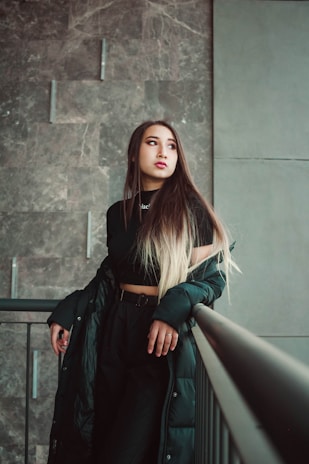 woman in black leather jacket standing beside gray concrete wall