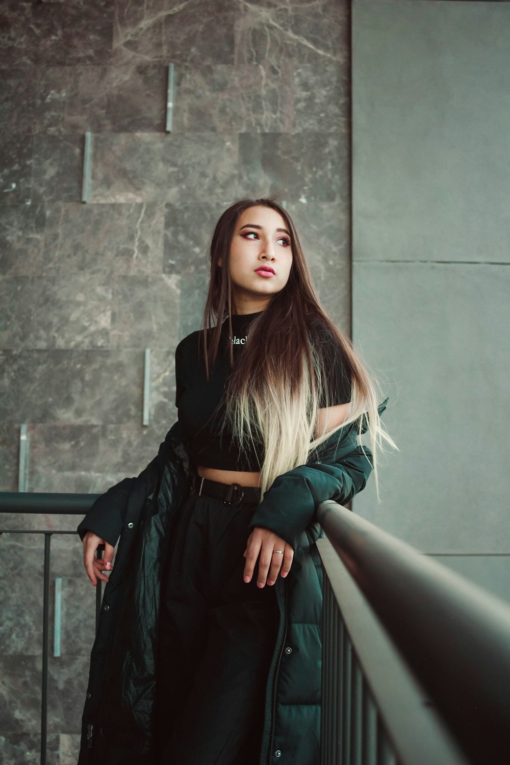 회색 콘크리트 벽 옆에 서 있는 검은 가죽 재킷을 입은 여자
