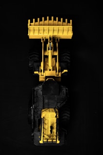 Close-up of a modern construction vehicle with a shiny yellow accent under bright lighting.