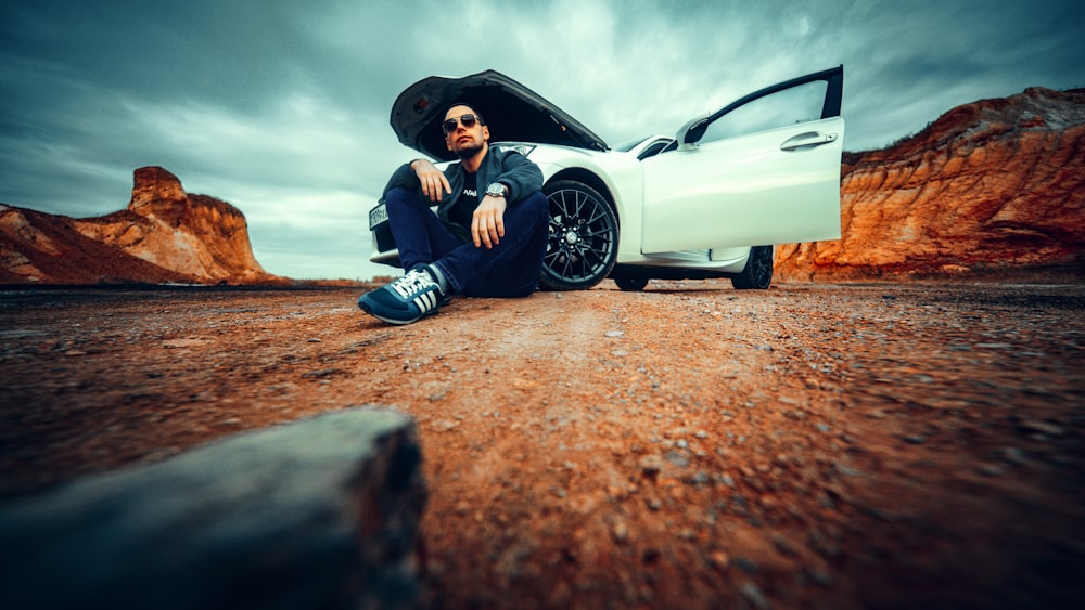 man in black jacket and black pants sitting on white car