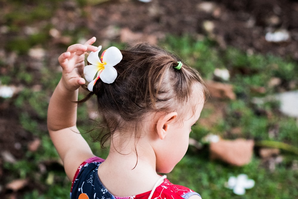 girl in red and blue floral dress holding white flower during daytime