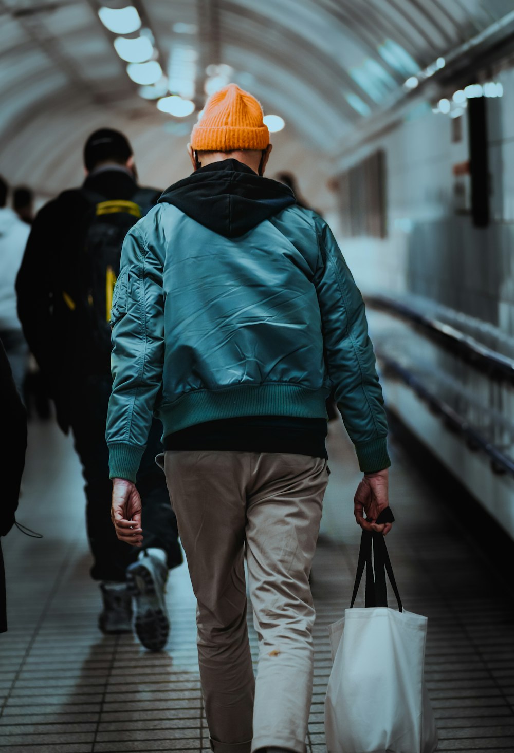 man in blue and orange jacket and gray pants walking on street during daytime