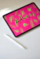 A tablet displaying the word 'Anxiety' in bold letters with a bright pink background and neon green scribbles. The tablet is placed on a white surface next to a white stylus pen.
