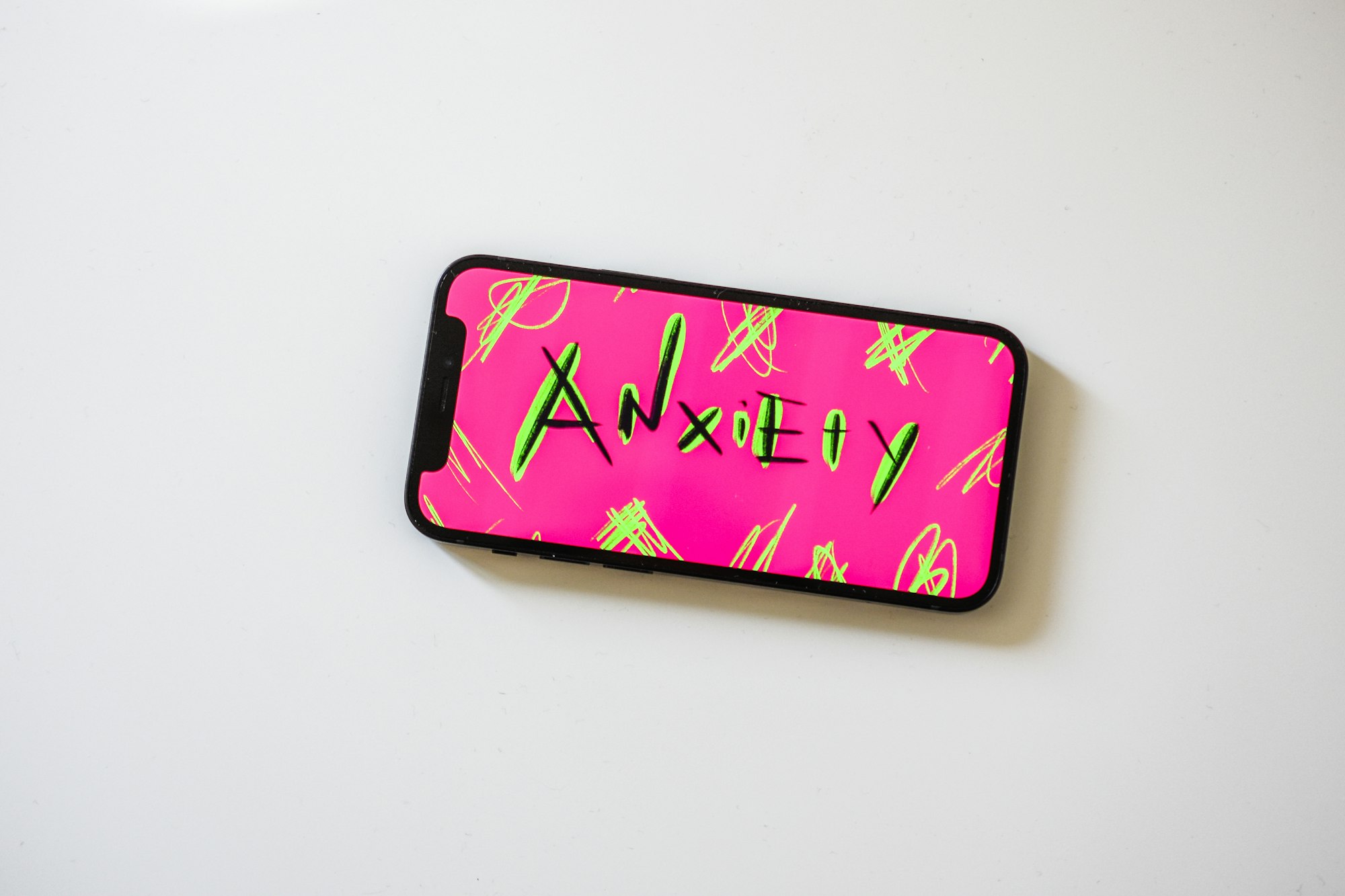 A cell phone with the work "anxiety" spelled on the front against a pink background