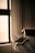A smartphone lies on a wooden table, connected to a charging cable. Soft ambient light filters through a window, casting a warm glow on the surroundings. In the background, curtains add a sense of calm and coziness to the scene.