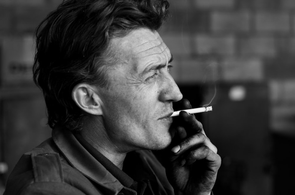 man smoking cigarette in grayscale photography