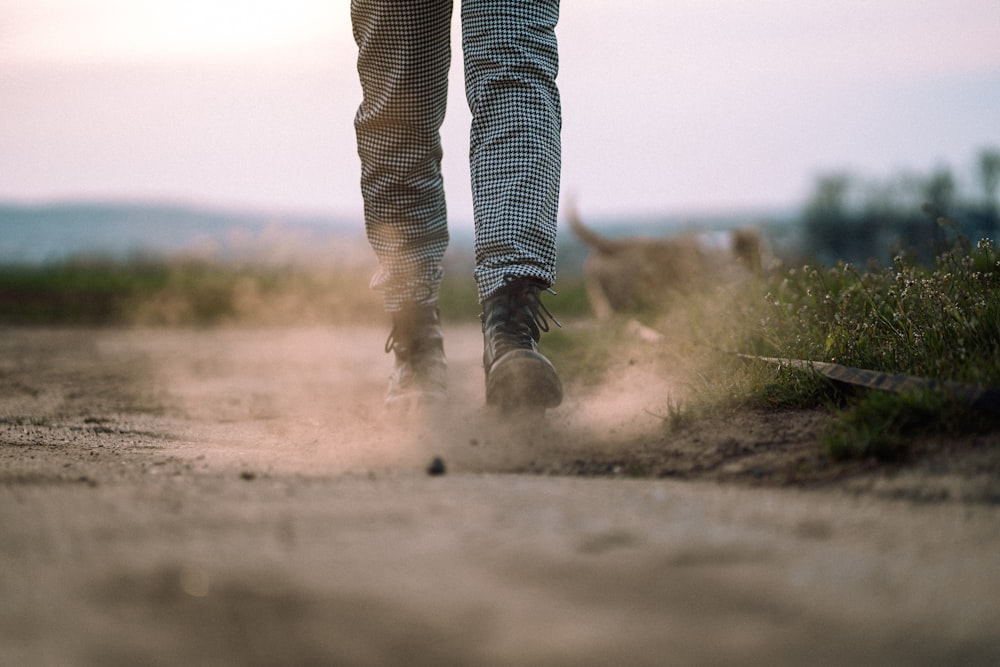 person in black and white striped pants walking on dirt road during daytime