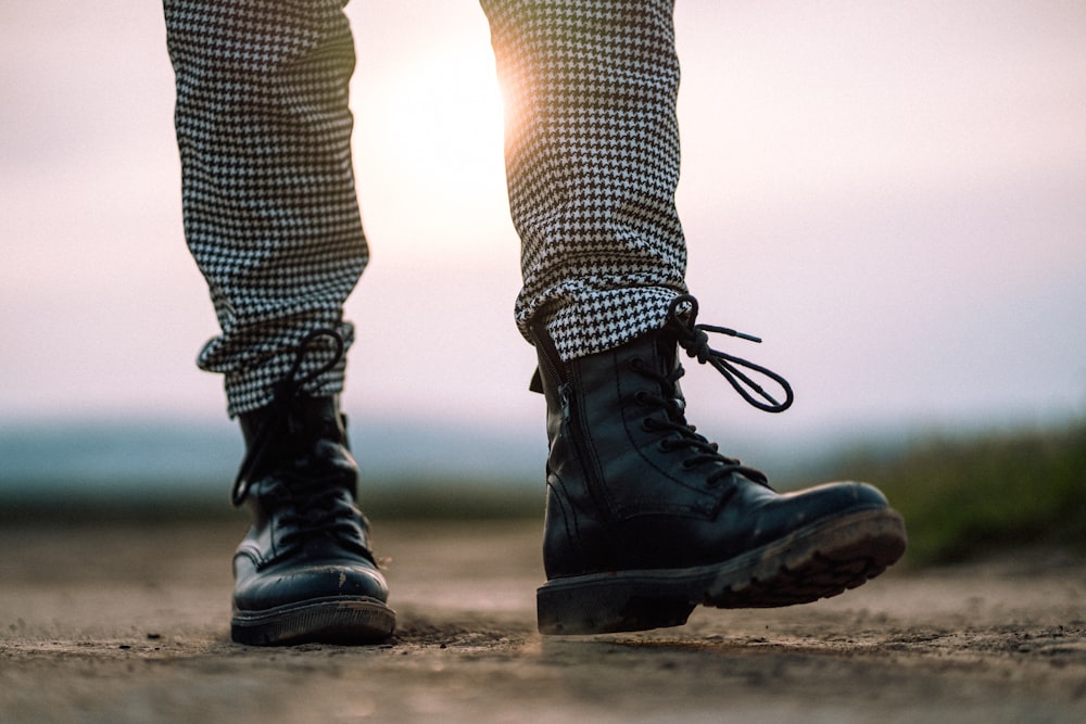 person in black leather boots standing on brown sand during daytime